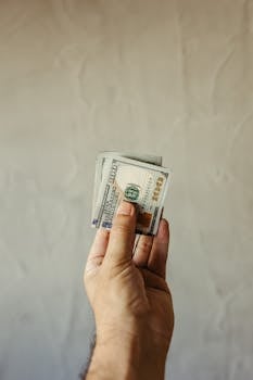 Close-up of a hand holding US dollar bills against a neutral background, symbolizing finance and economy.